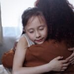 Mama obejmuje córkę w domu w trudnym dla rodziny czasie zmian