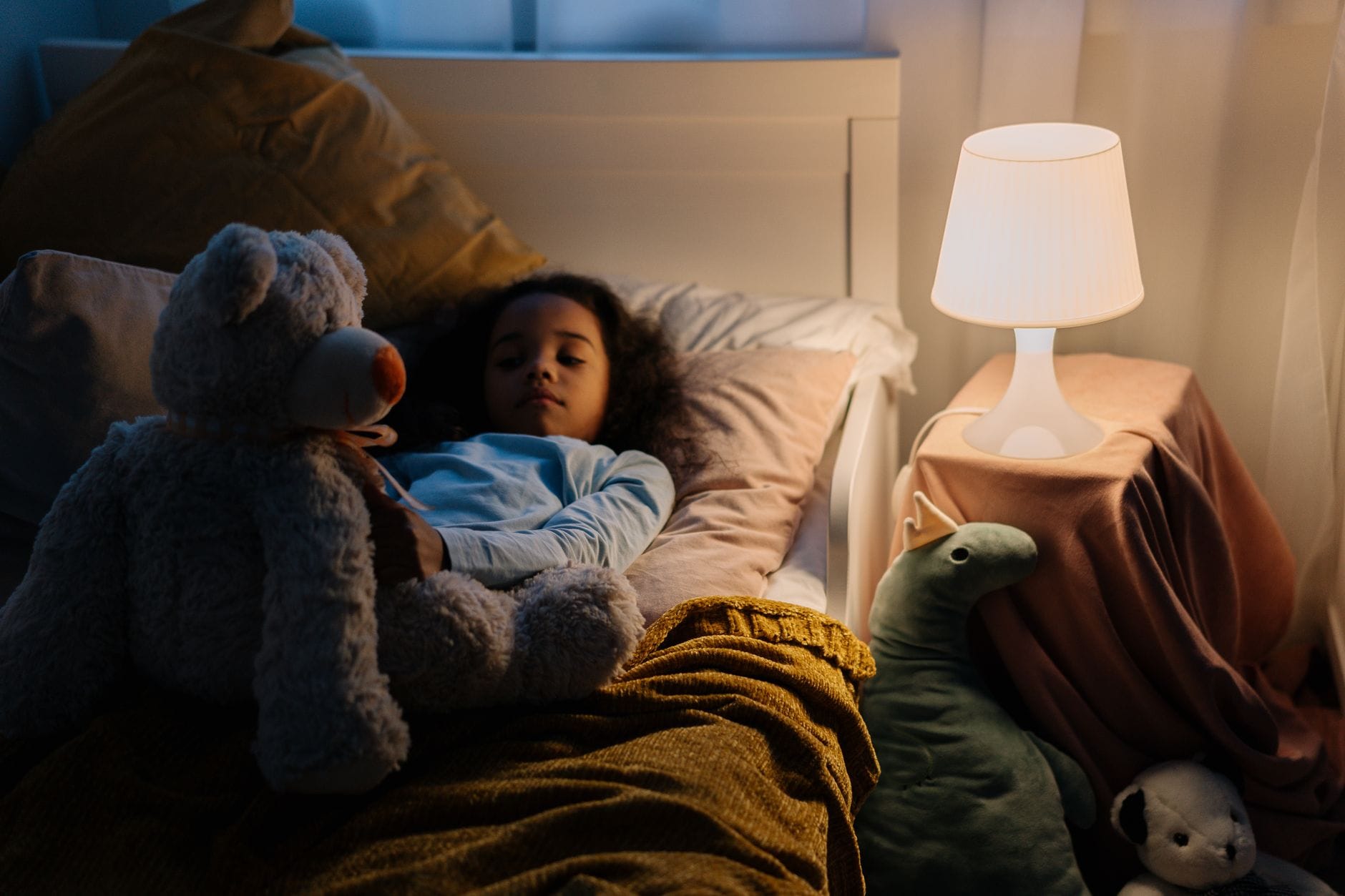 Dziewczynka odpoczywa w łóżku z misiem przy lampce nocnej
