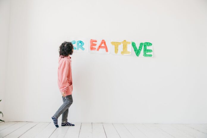 Dziecko maluje kolorowy napis CREATIVE na białej ścianie
