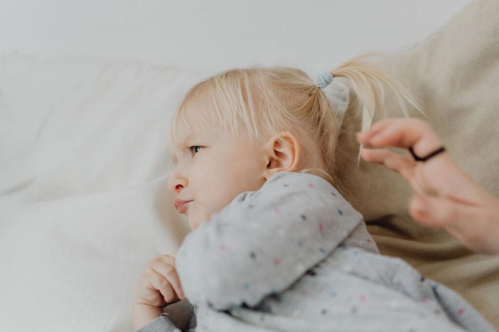 Naburmuszona blond dziewczynka z kucykiem siedząca na łóżku